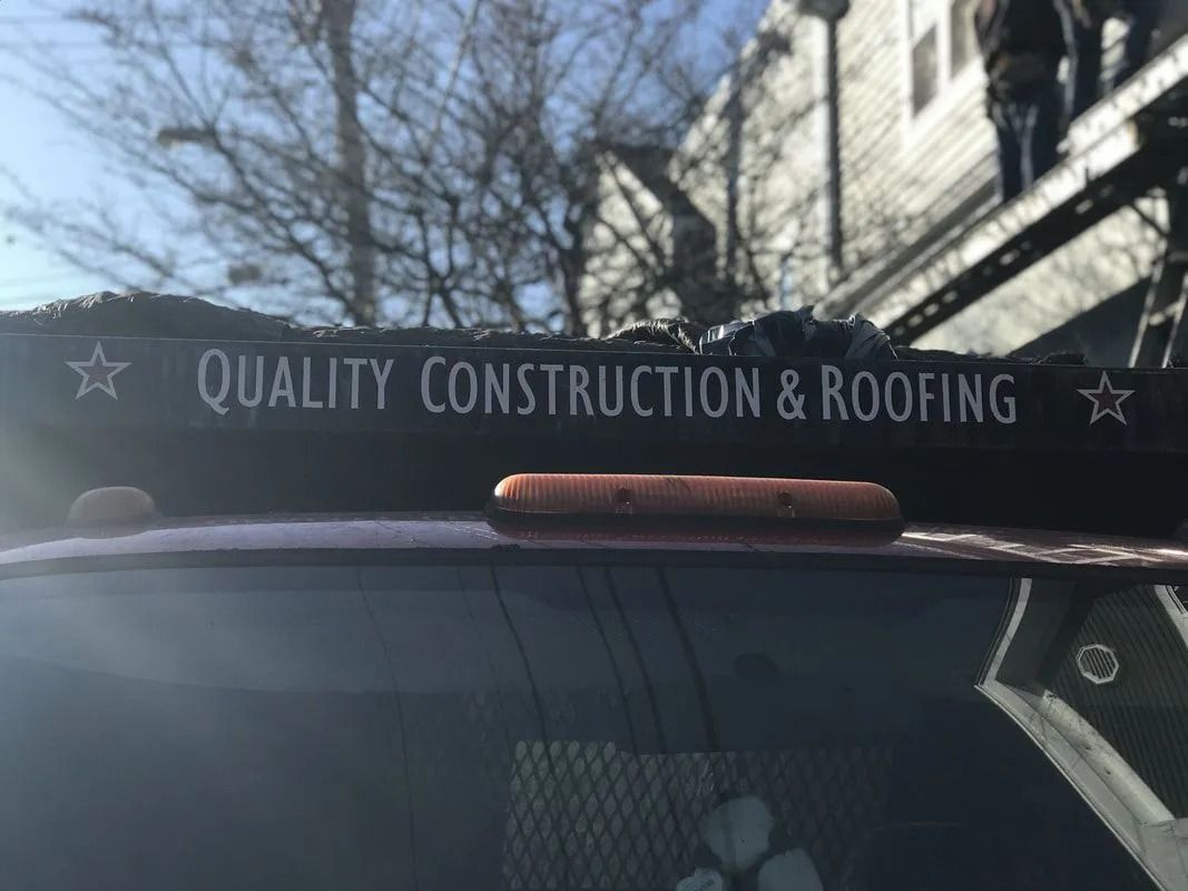 A black sign reading "QUALITY CONSTRUCTION & ROOFING" with stars on each side, mounted on a vehicle near a building.