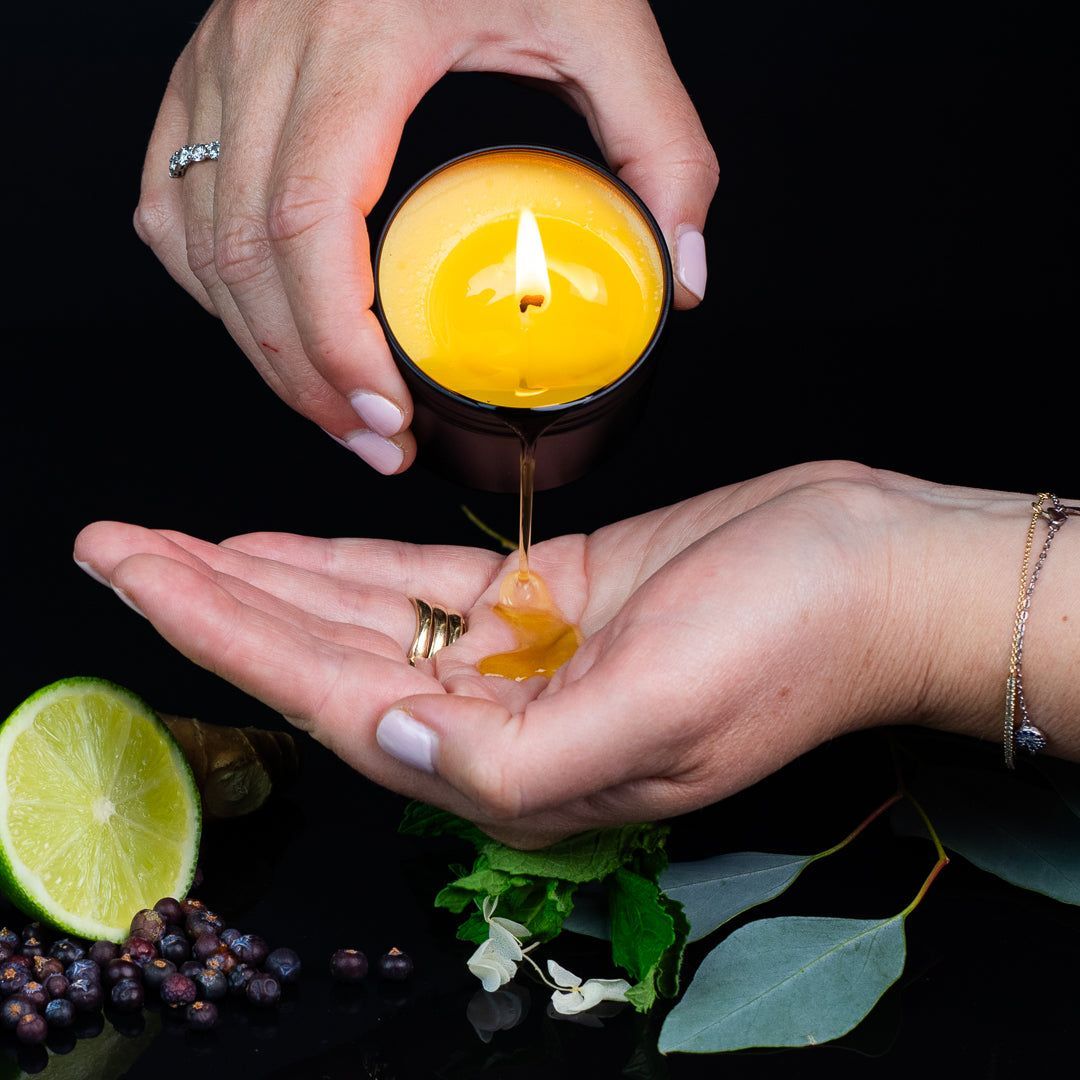 Hands holding candle, pouring wax into a cupped palm with ring. Lime, berries, herbs in dark setting.