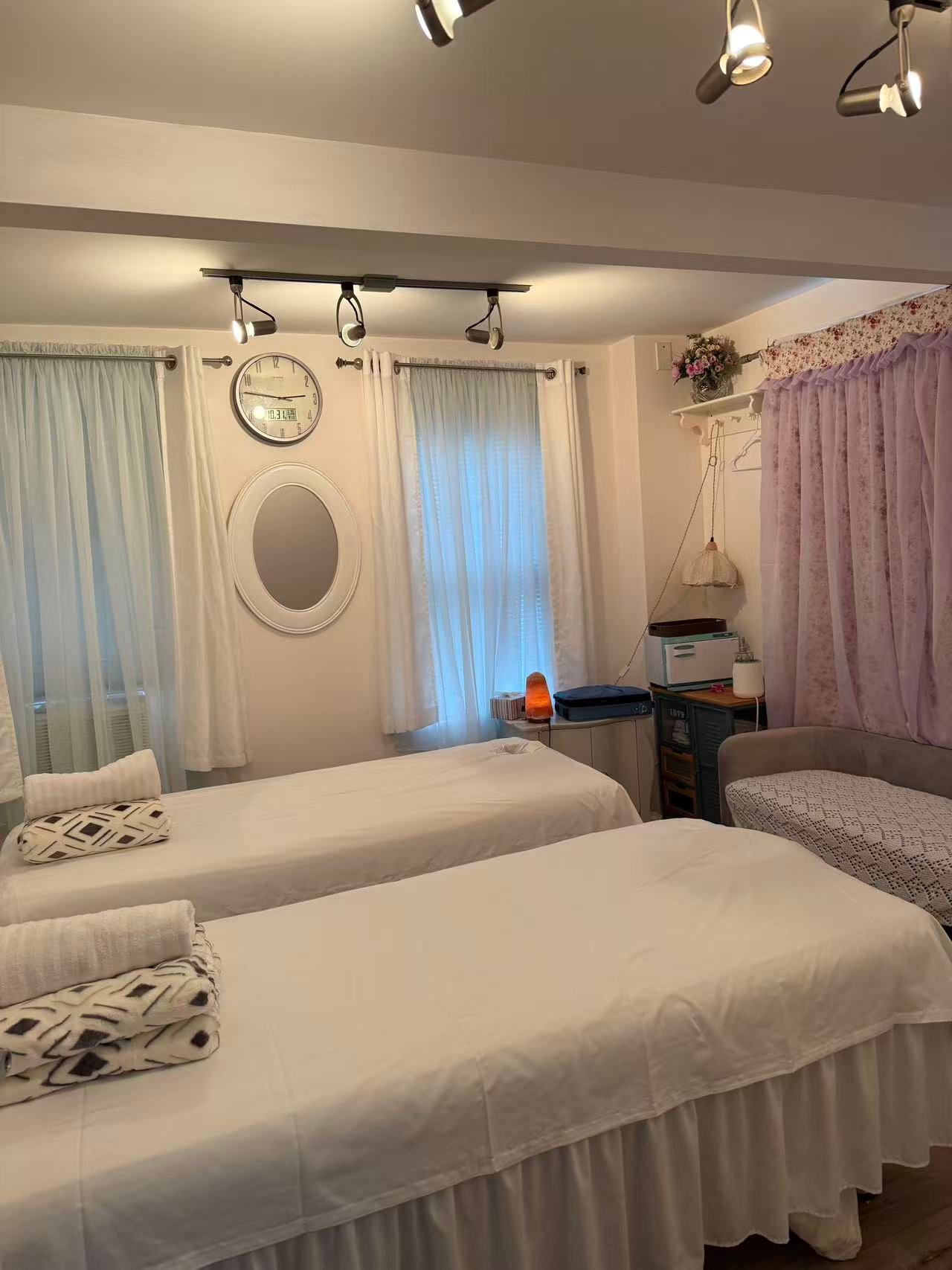 Massage room with two beds, white linens, soft lighting, and decorative curtains.