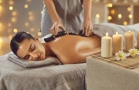 Woman receiving hot stone massage at spa. Candles and flowers on the table.