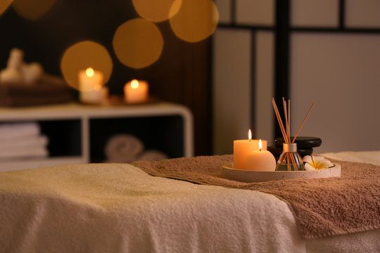 Massage table with candle, diffuser, and towels in a dimly lit spa setting.
