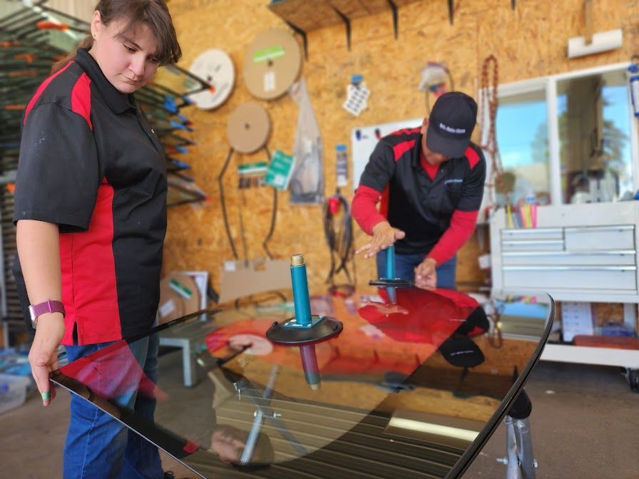 A man and a woman are working on a windshield in a garage.