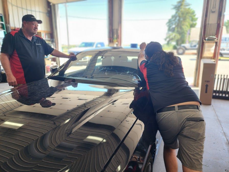 A man and a woman are working on a car windshield
