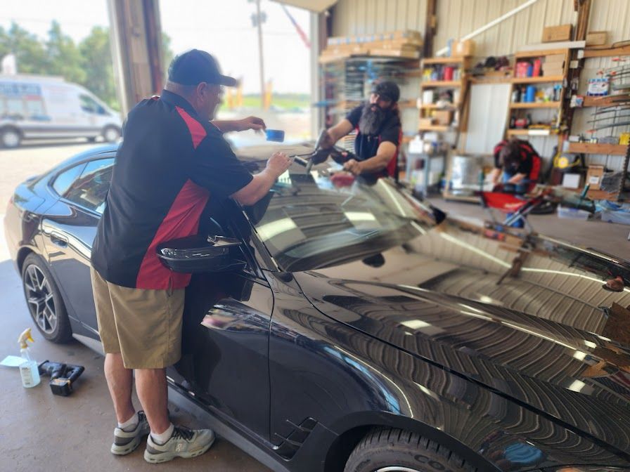 Two men are working on a car windshield in a garage.