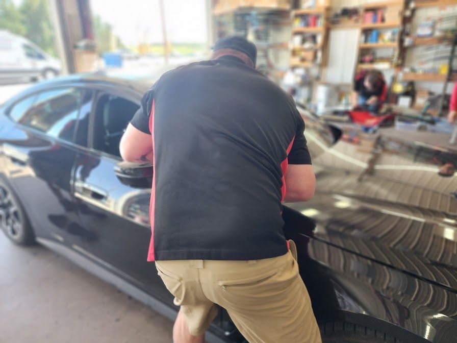 A man in a black shirt is standing next to a black car