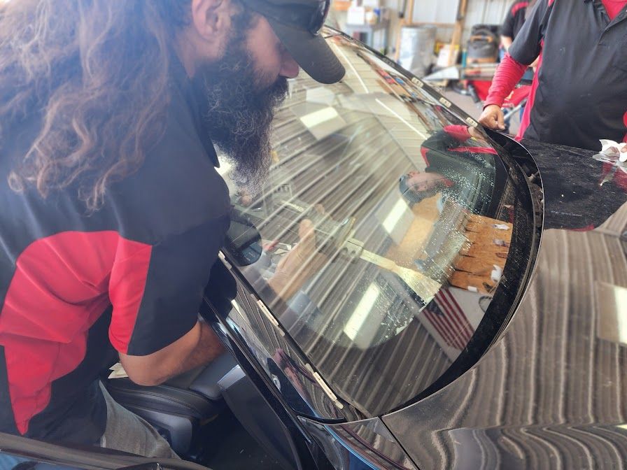 A man with a beard is working on a car windshield.