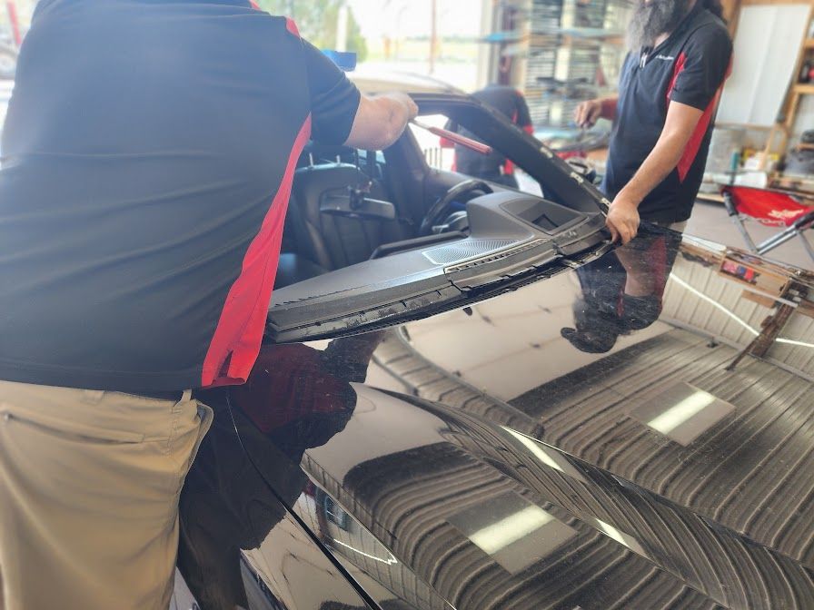 Two men are working on a car windshield in a garage.