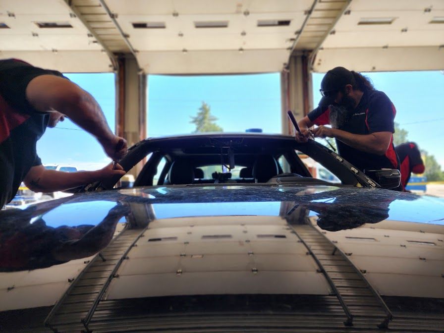 Two men are working on a car windshield in a garage.