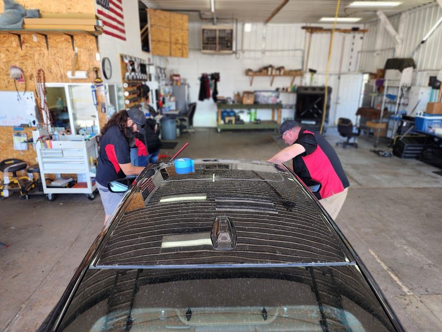 Two men are working on the roof of a car in a garage