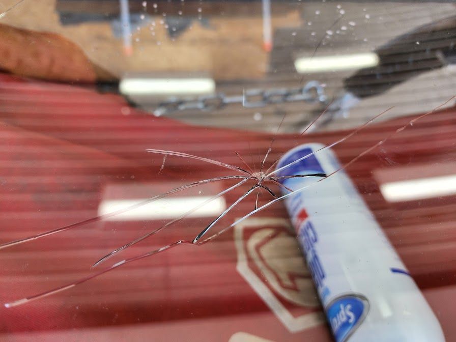 A bottle of toothpaste is sitting on a cracked windshield.