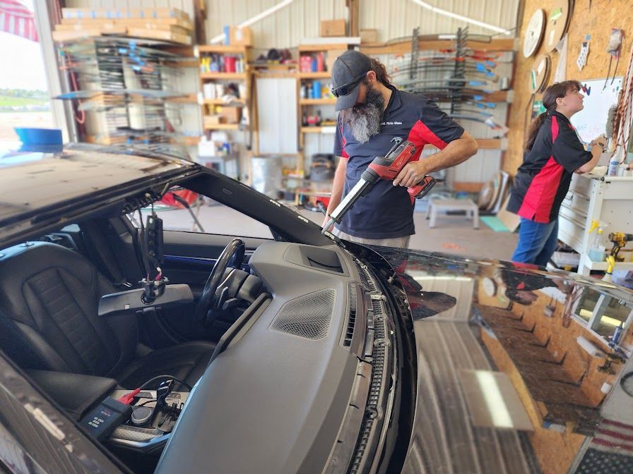 A man is installing a windshield on a car in a garage.