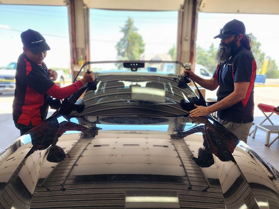 Two men are working on a car windshield in a garage.