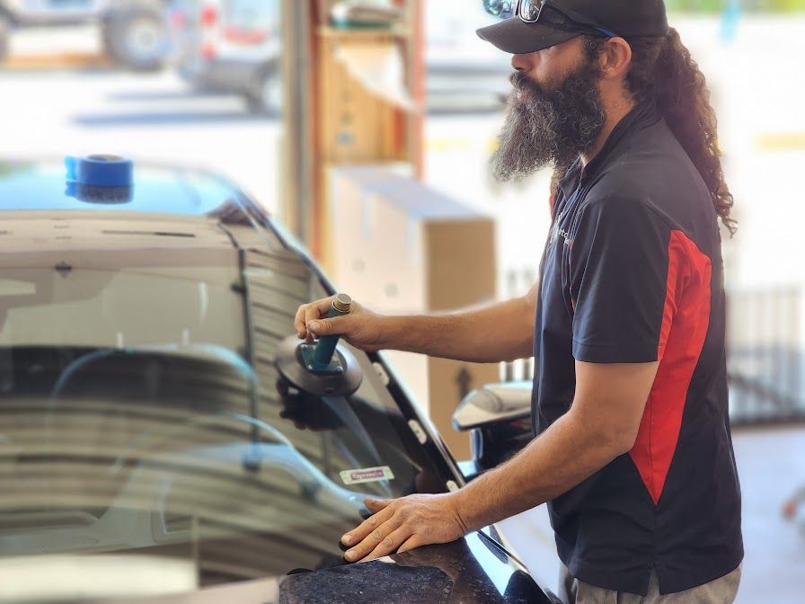 A man with a beard is fixing a windshield on a car.