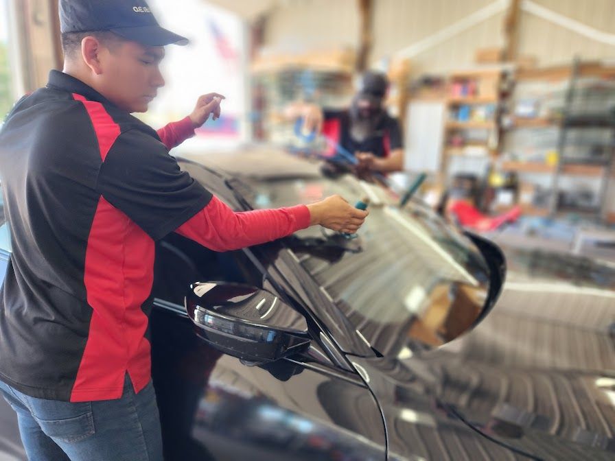 A man in a red and black shirt is working on a car windshield