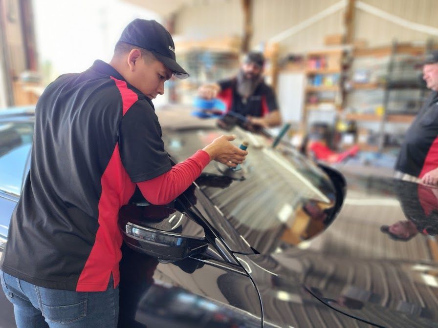 A man is working on a car windshield in a garage.