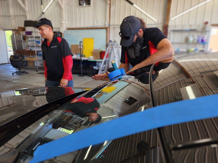 Two men are working on a car windshield in a garage.