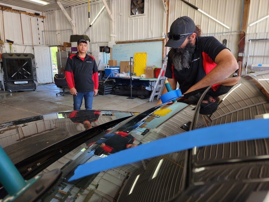 A man is working on a windshield of a car in a garage.