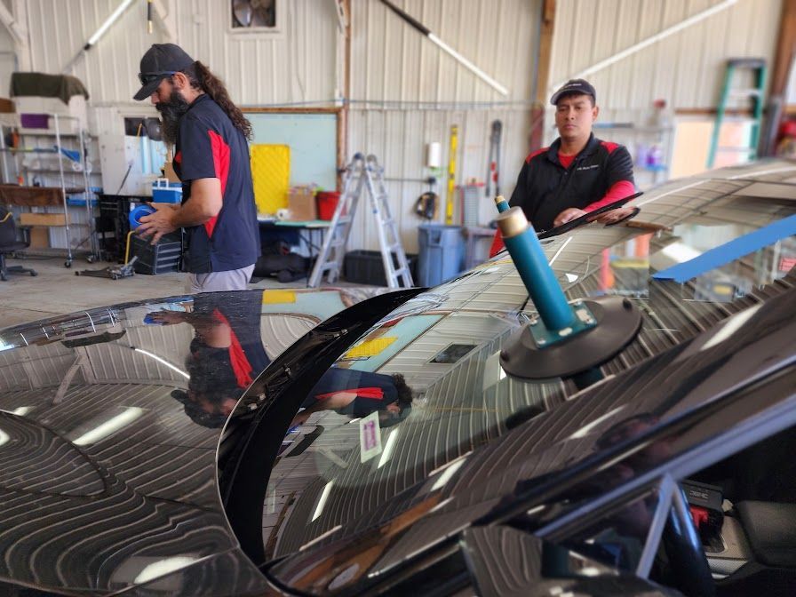 Two men are working on a car windshield in a garage