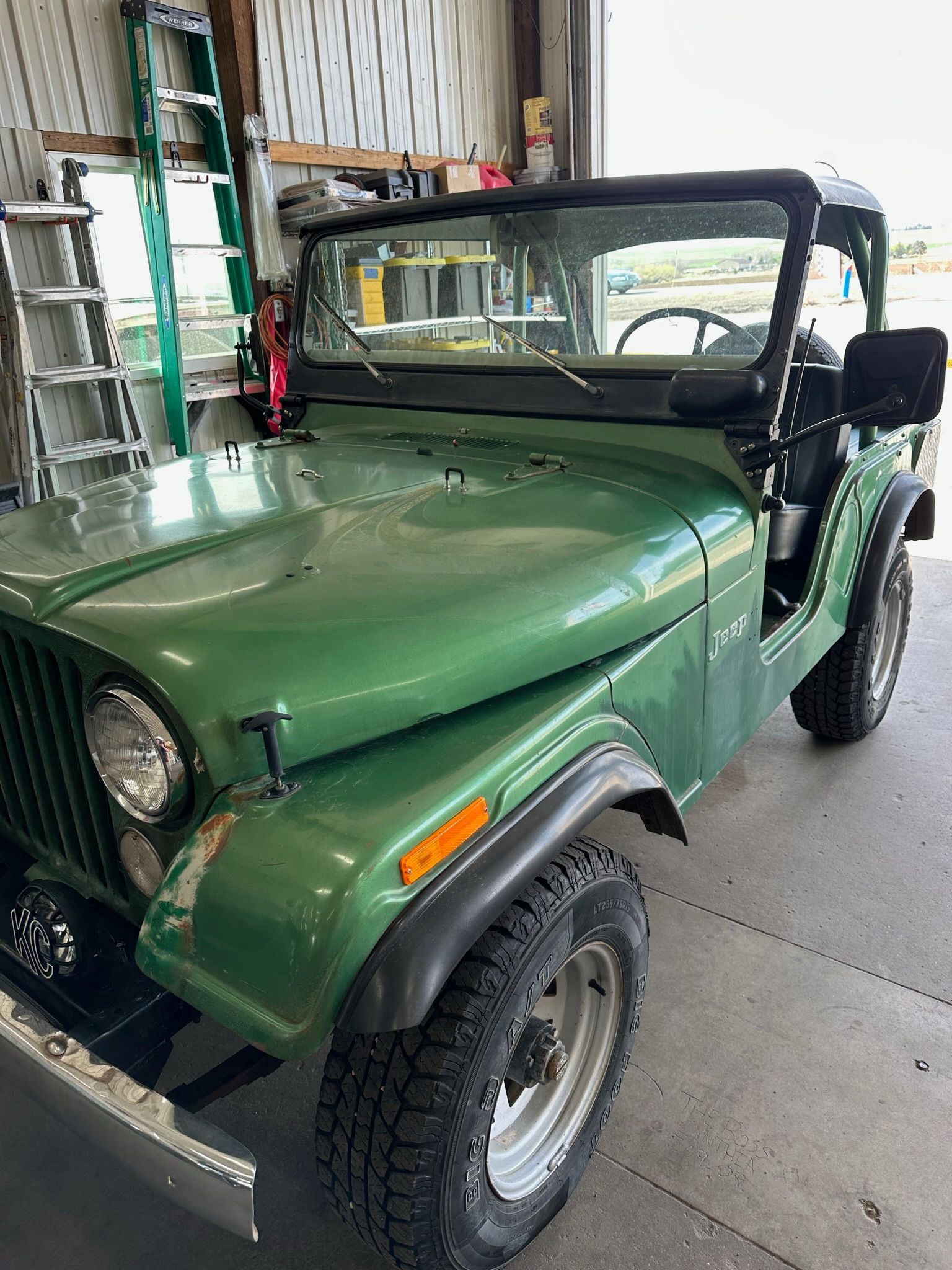 A green jeep is parked in a garage next to a ladder.