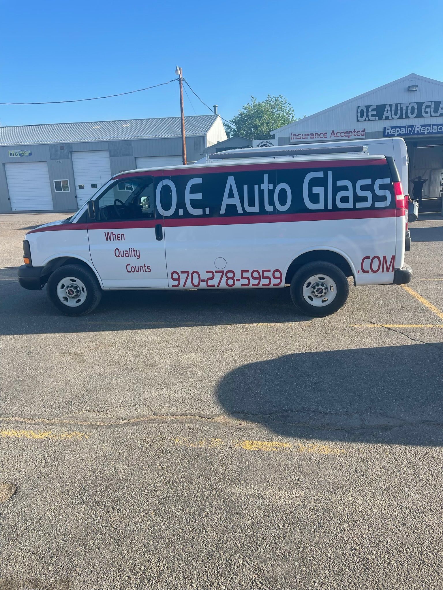 A white van is parked in front of a building that says o.e. auto glass.