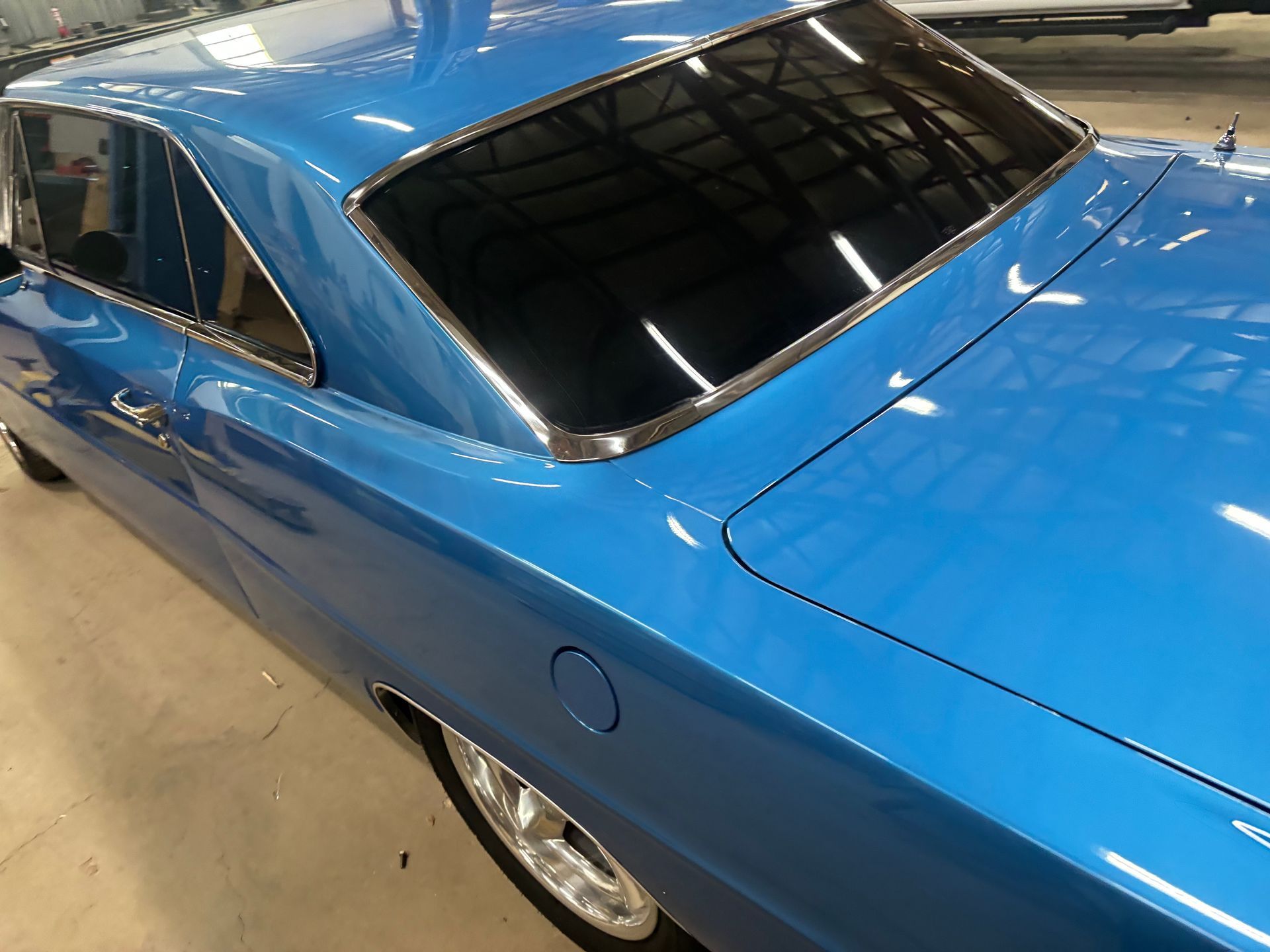 A blue car with a chrome trim is parked in a garage