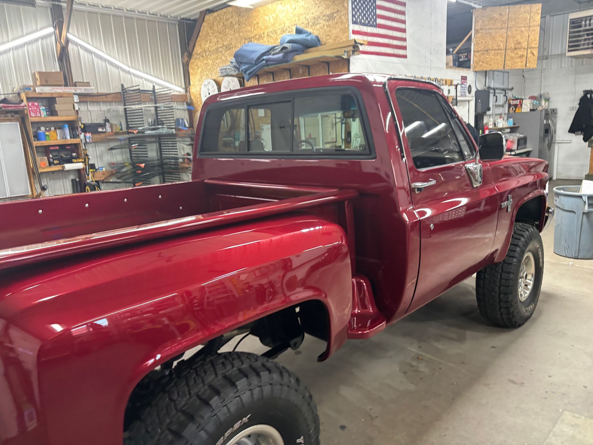 A red truck is parked in a garage next to an american flag.
