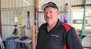 A man in a black and red shirt and hat is standing in a garage.