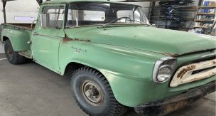An old green pickup truck is parked in a garage.