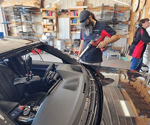 A man is fixing a windshield on a car in a garage.