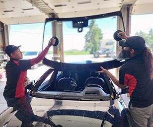 Two men are installing a windshield on a car.