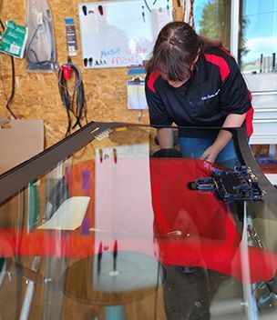 A woman is working on a windshield in a garage.