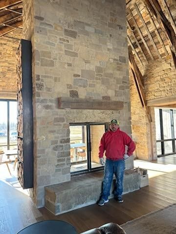 A man in a red jacket is standing in front of a large stone fireplace