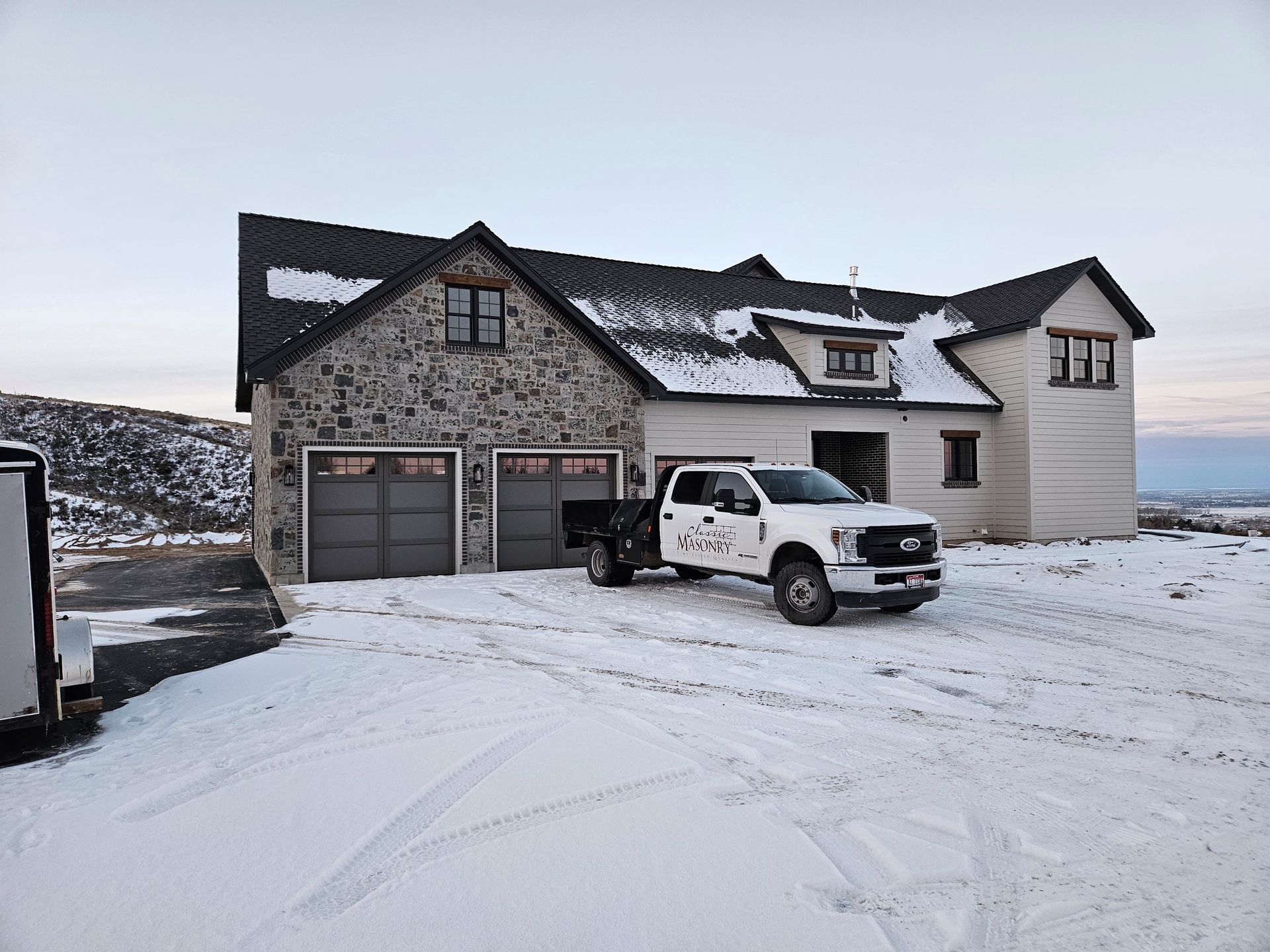 A white truck is parked in front of a large house in the snow