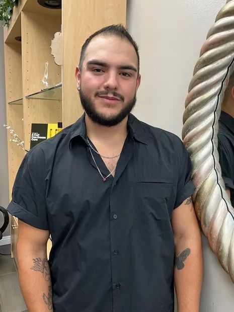 Man with beard, in black shirt, standing in salon setting.