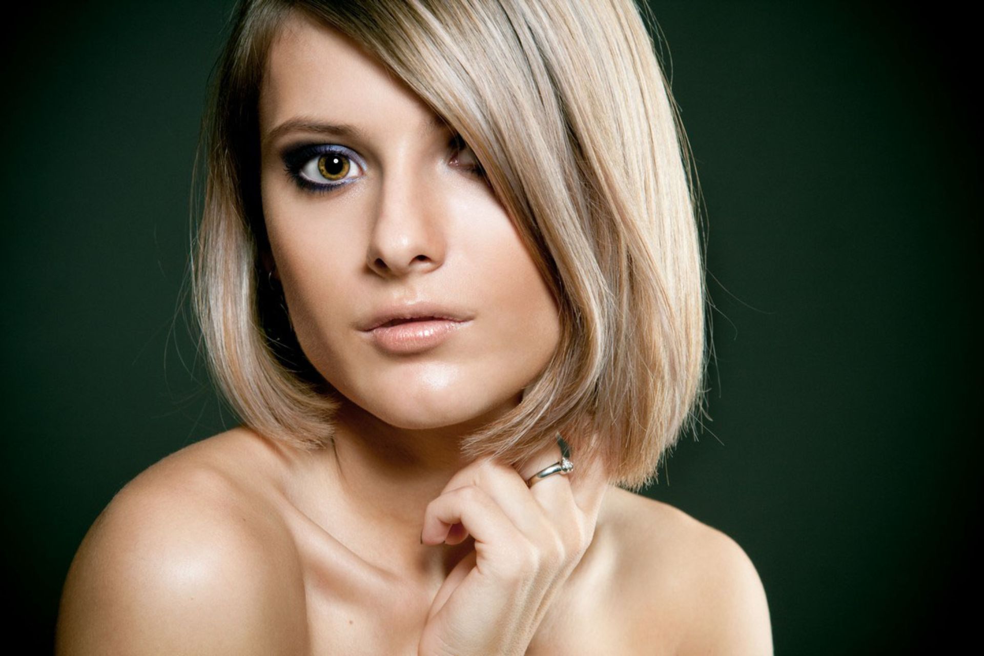 Woman with short blonde hair, smoky eye makeup, looking at the camera, dark background.