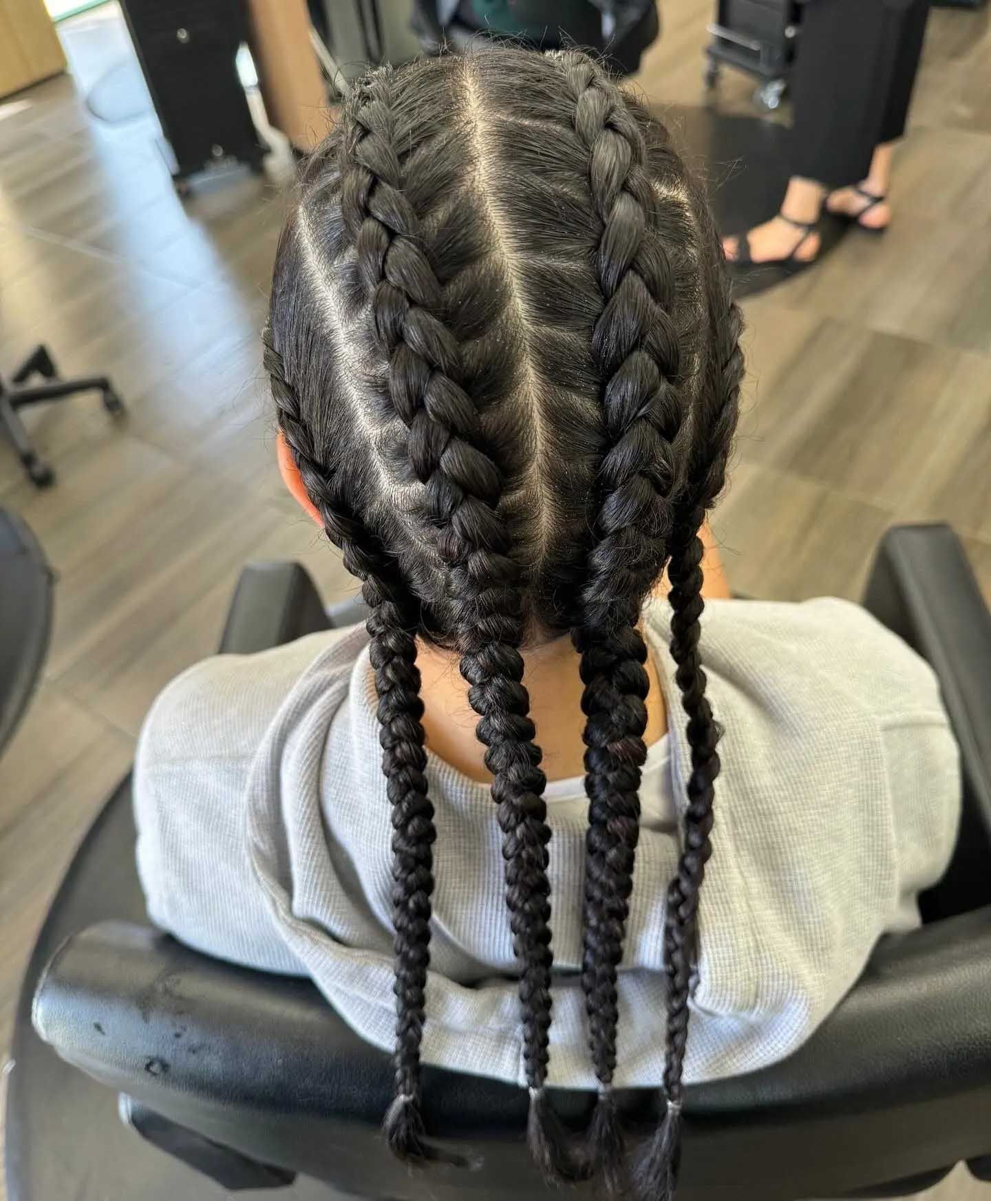 Close-up of person with dark hair in cornrows. Braids cascade down back. In salon setting.