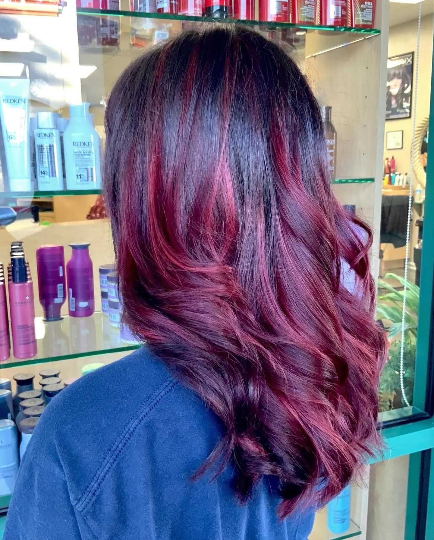 Woman with dark hair and vibrant burgundy highlights, styled in loose waves.
