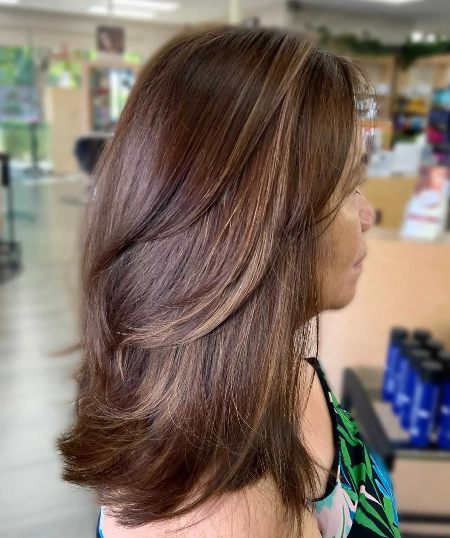 Woman with layered brown hair and highlights, in a salon.