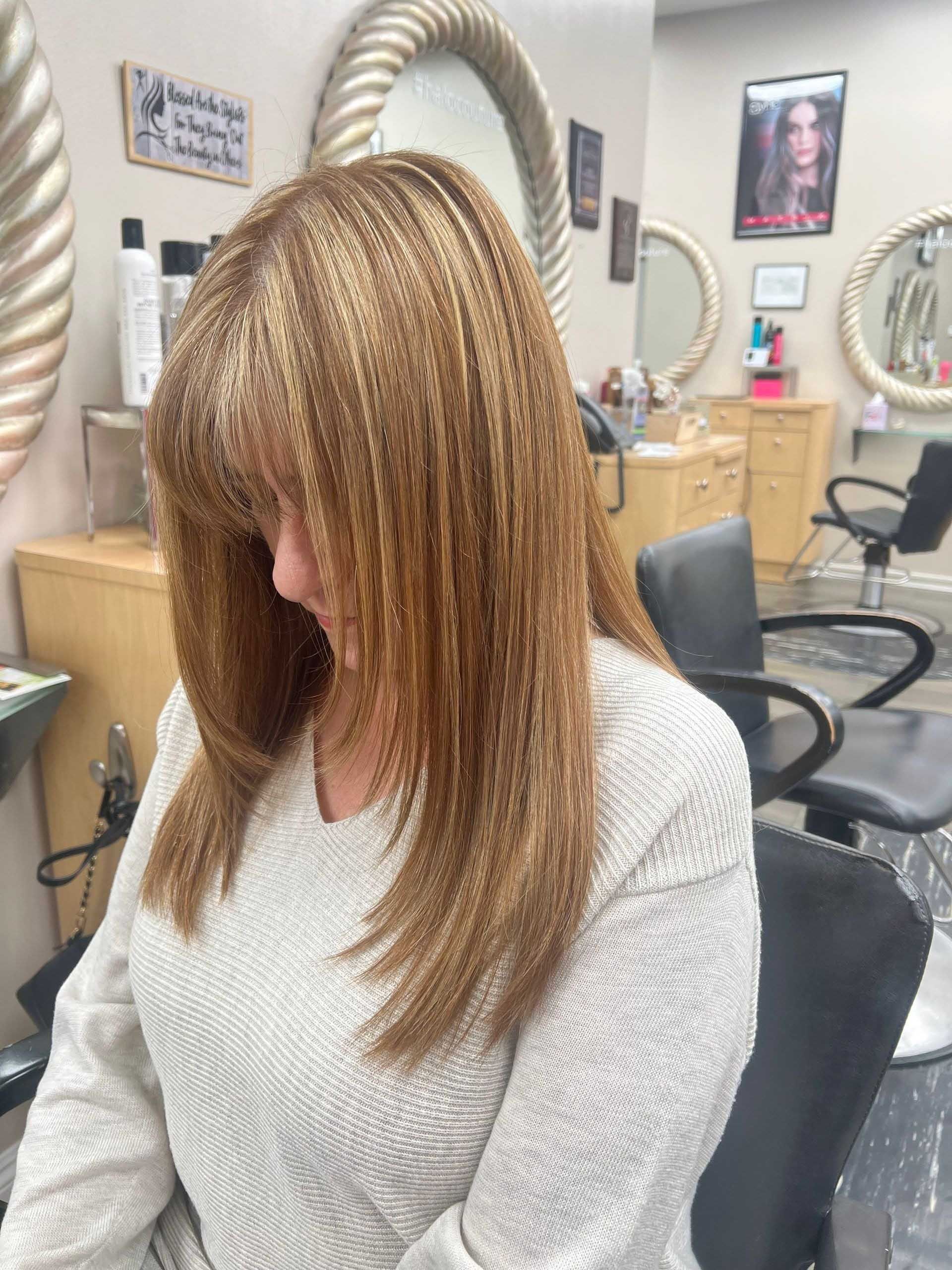 Woman with crimped, light brown hair in a salon, wearing a white sweater.
