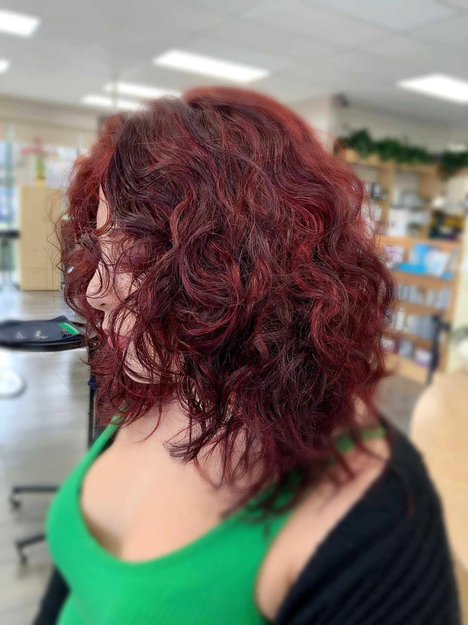 Woman with curly, red hair in a green top and black cardigan, in a salon.