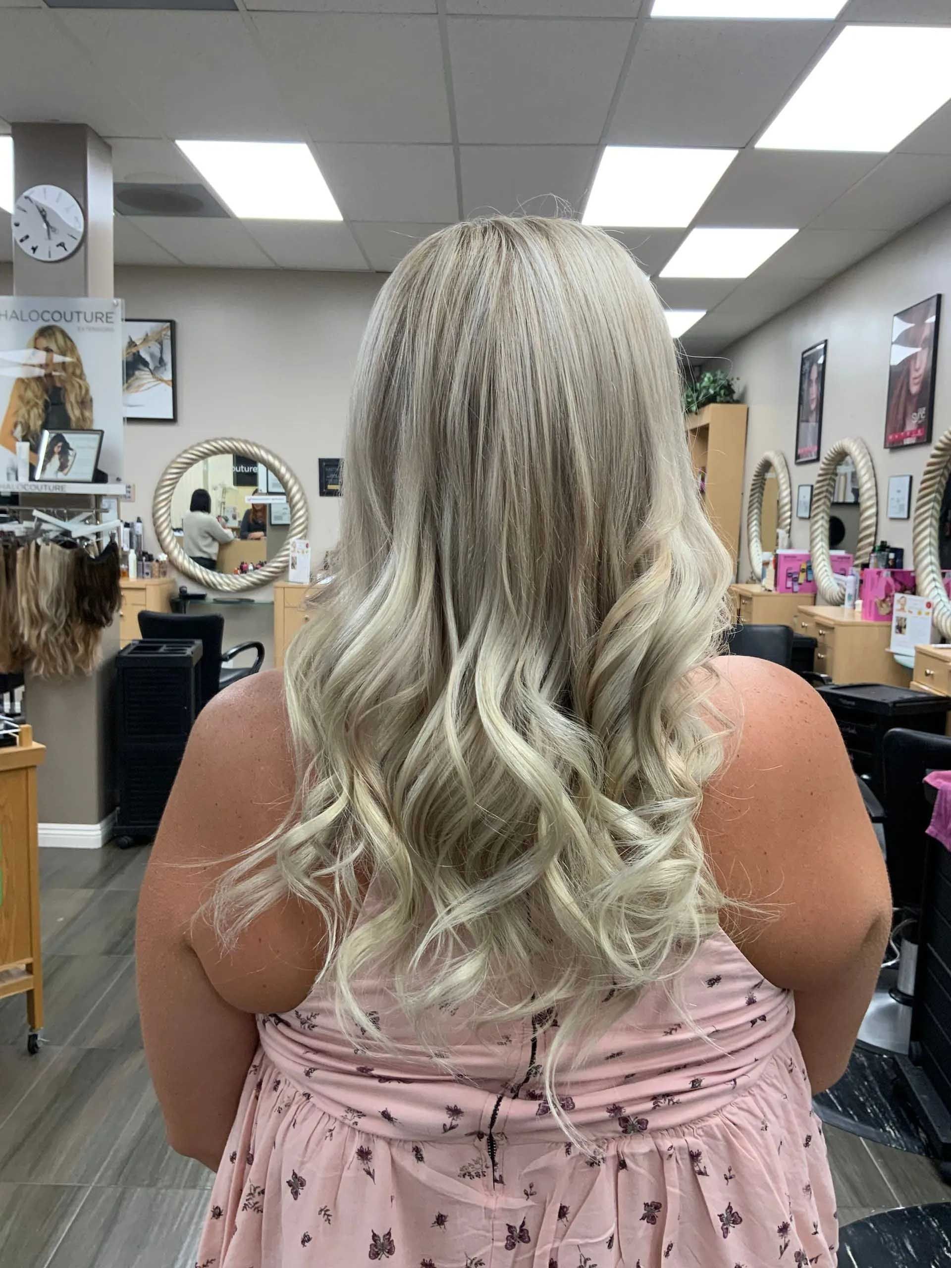 Woman with blonde wavy hair at a salon, wearing a pink dress.