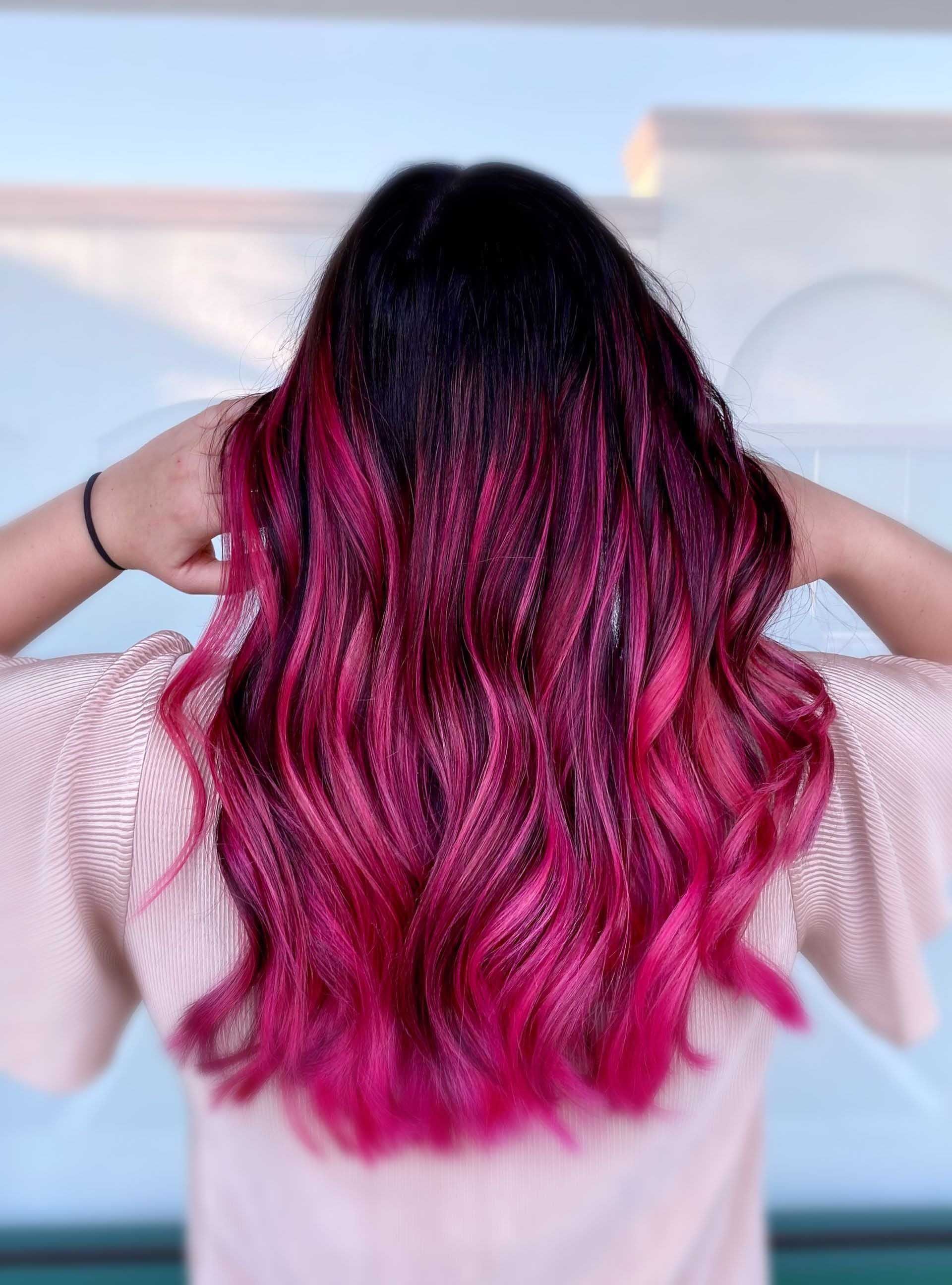 Woman with dark hair transitioning to vibrant pink waves, hands behind head.