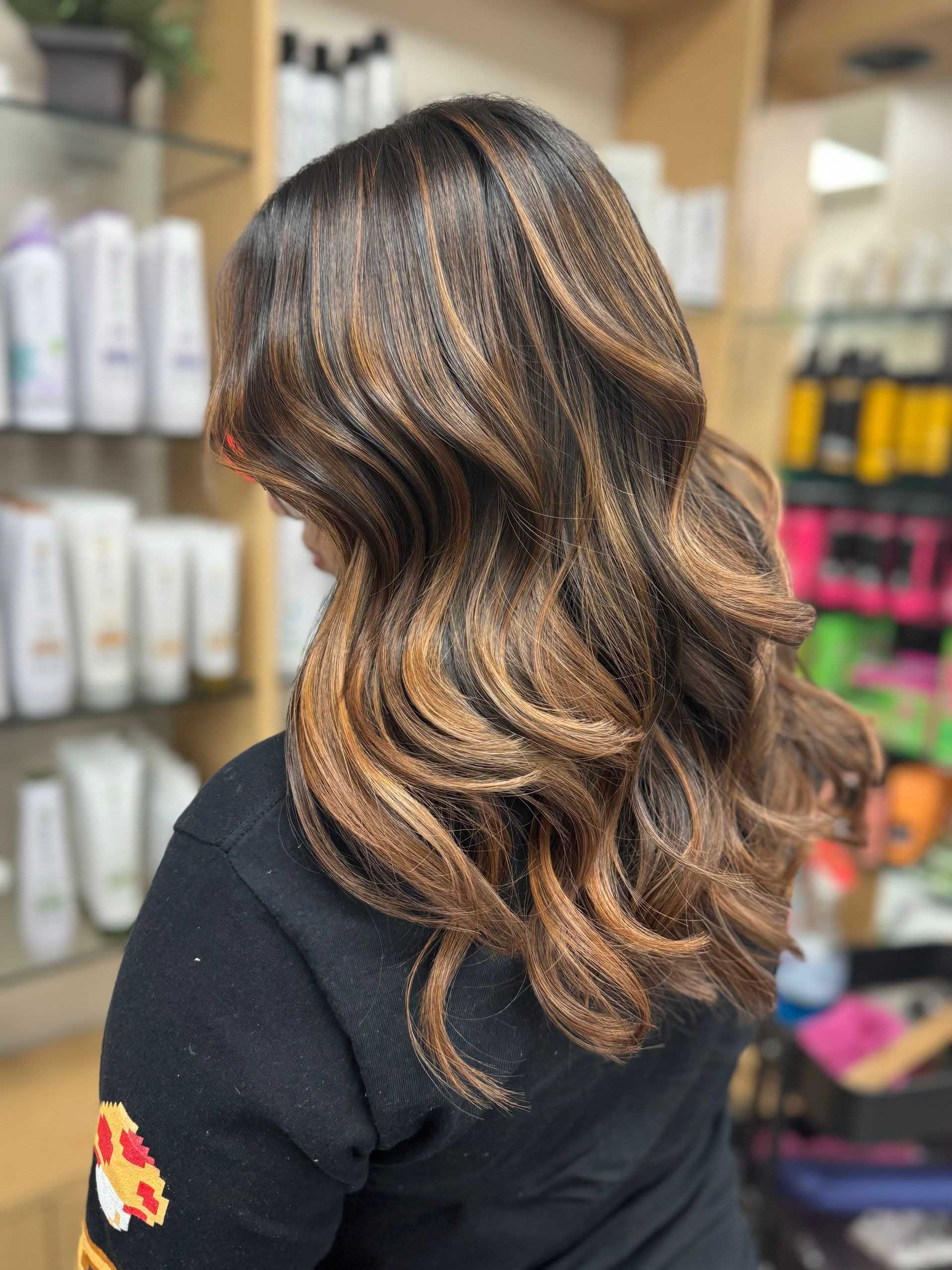 Woman with wavy, dark brown hair with caramel highlights, styled in a salon.