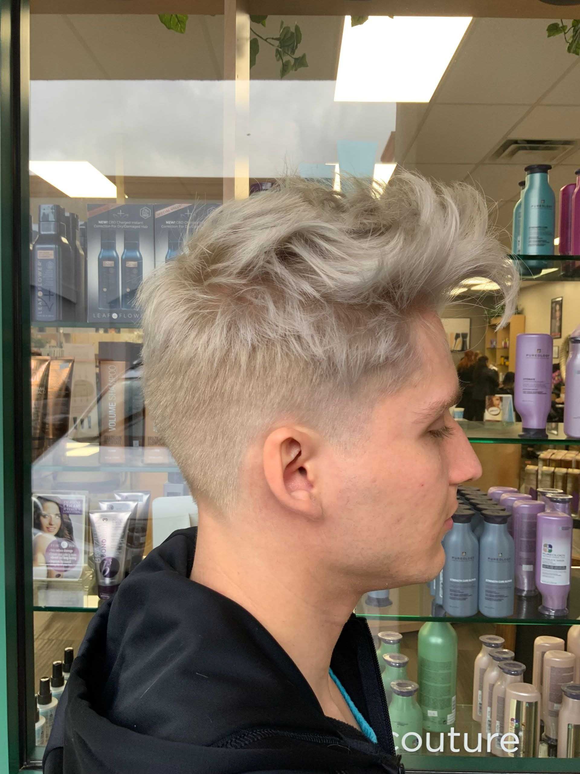 Man with light blonde, textured hair and a faded haircut, in a salon.