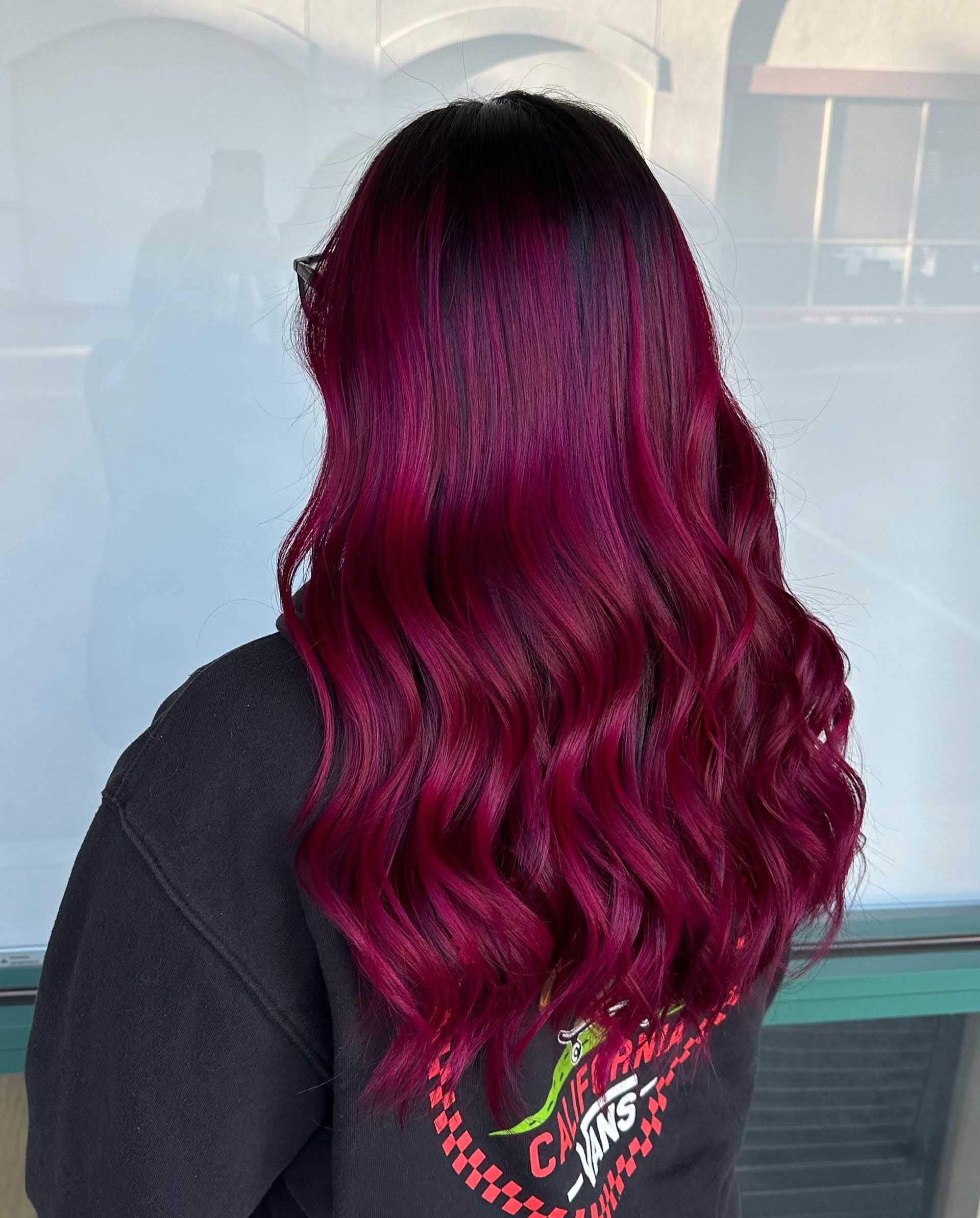 Woman with long, wavy, dark red hair, wearing a black shirt with a graphic.