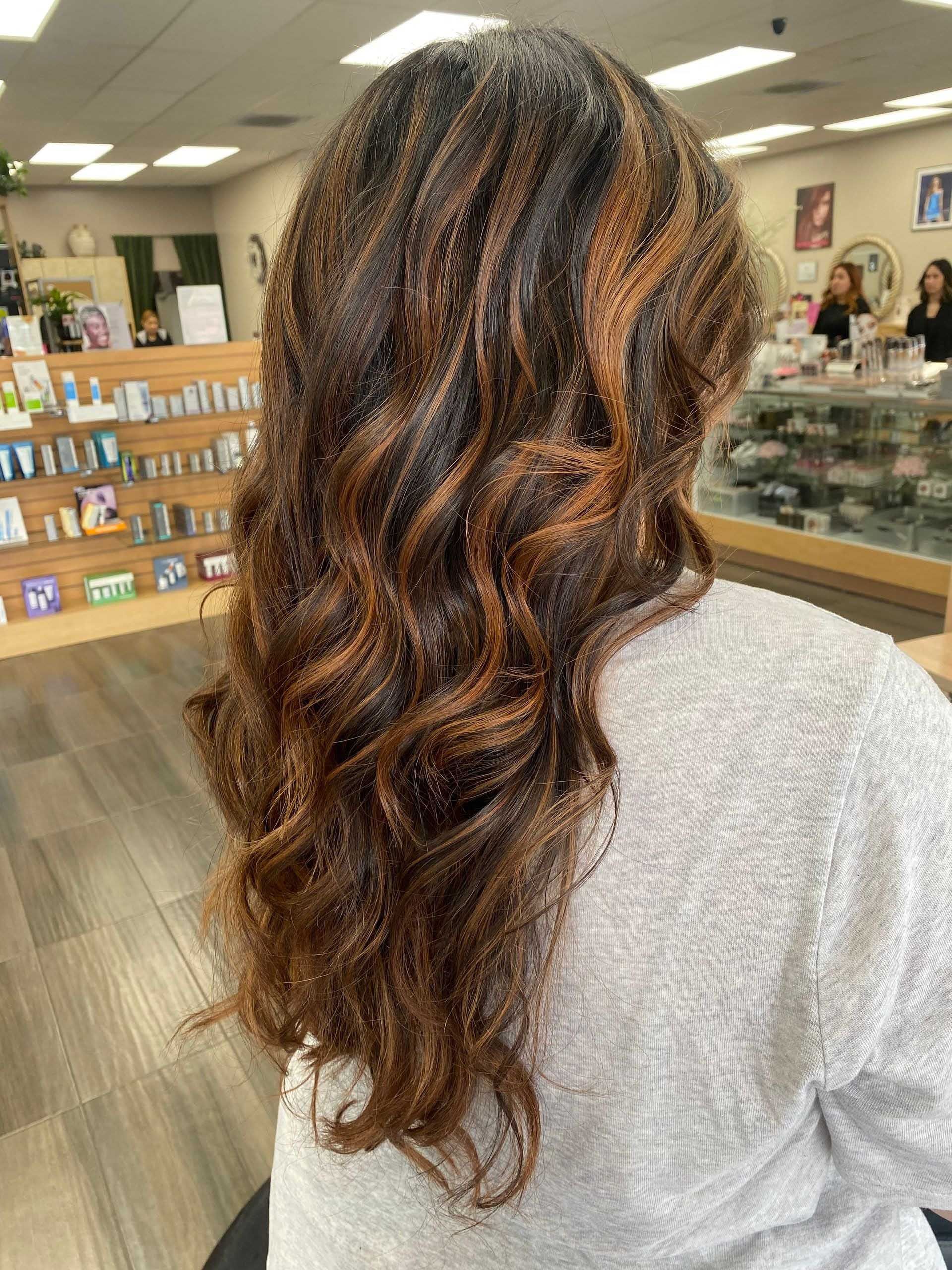 Woman with long, wavy brown hair with reddish highlights, sitting in a salon.