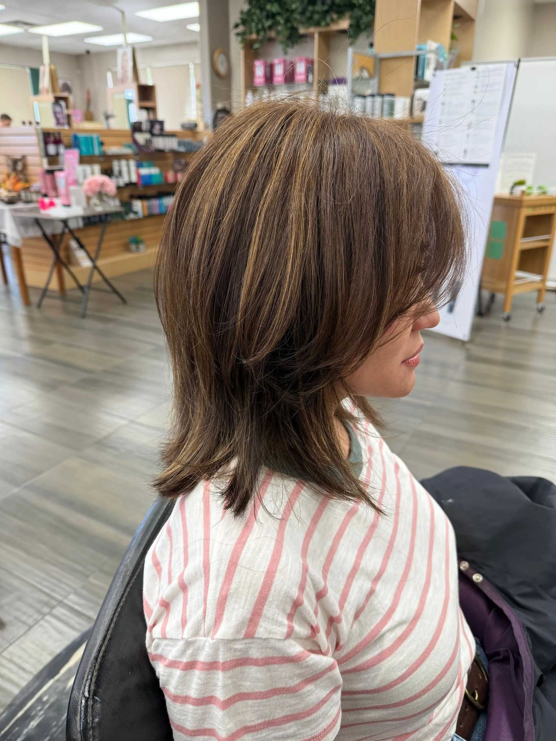 Woman with layered brown hair in a salon, wearing a striped shirt, profile view.