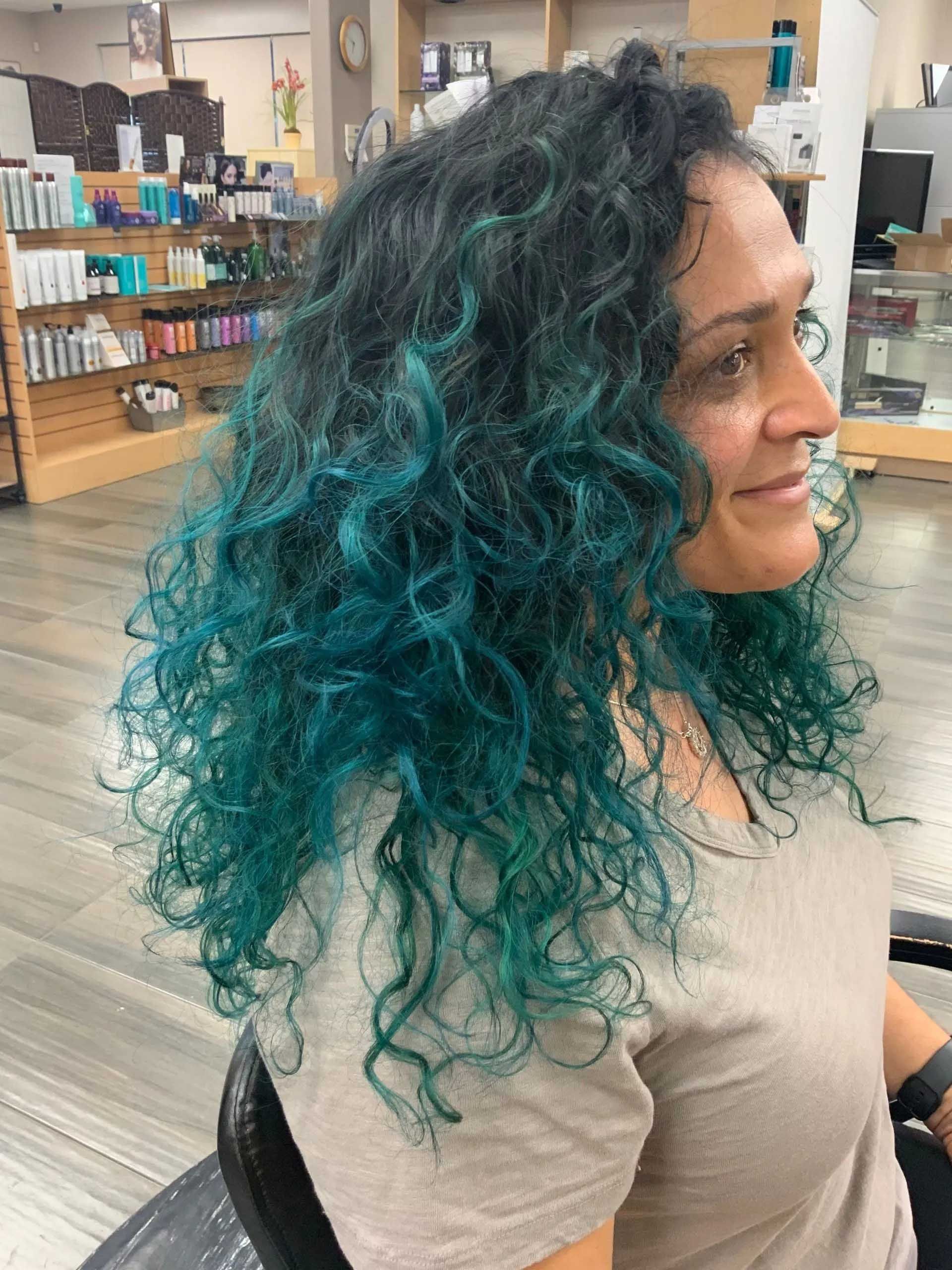 Woman with curly hair, teal dye on ends, smiling in a salon.
