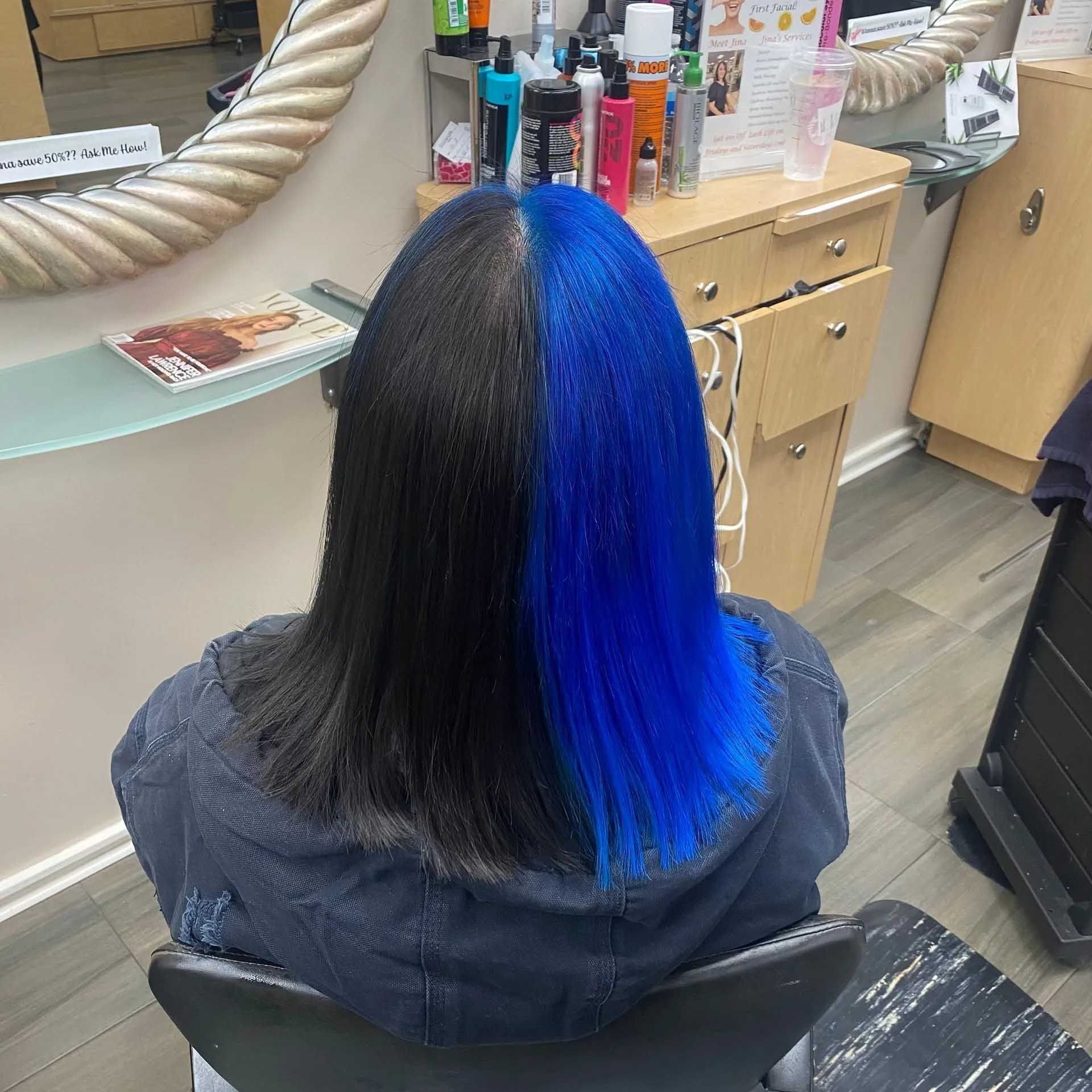 Hair parted down the middle, half black and half blue, in a salon chair.
