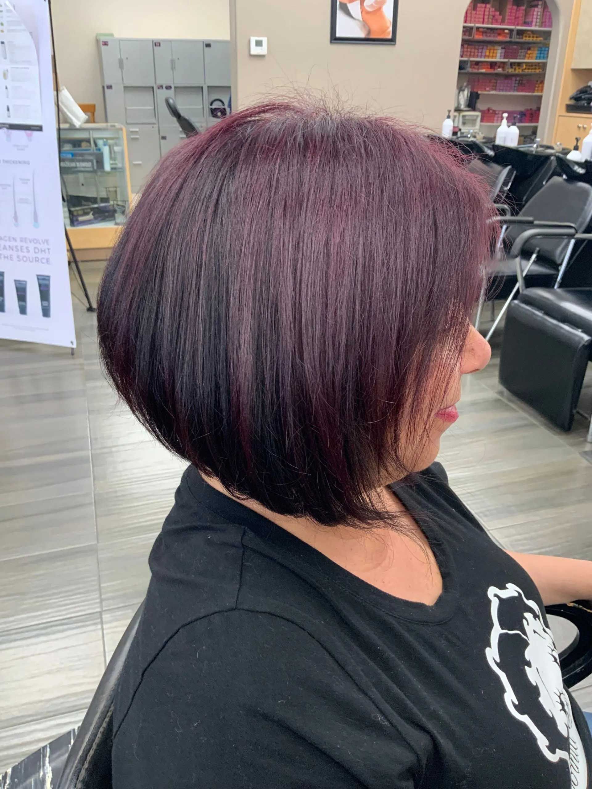 Woman with a dark purple bob haircut in a salon, wearing a black shirt.